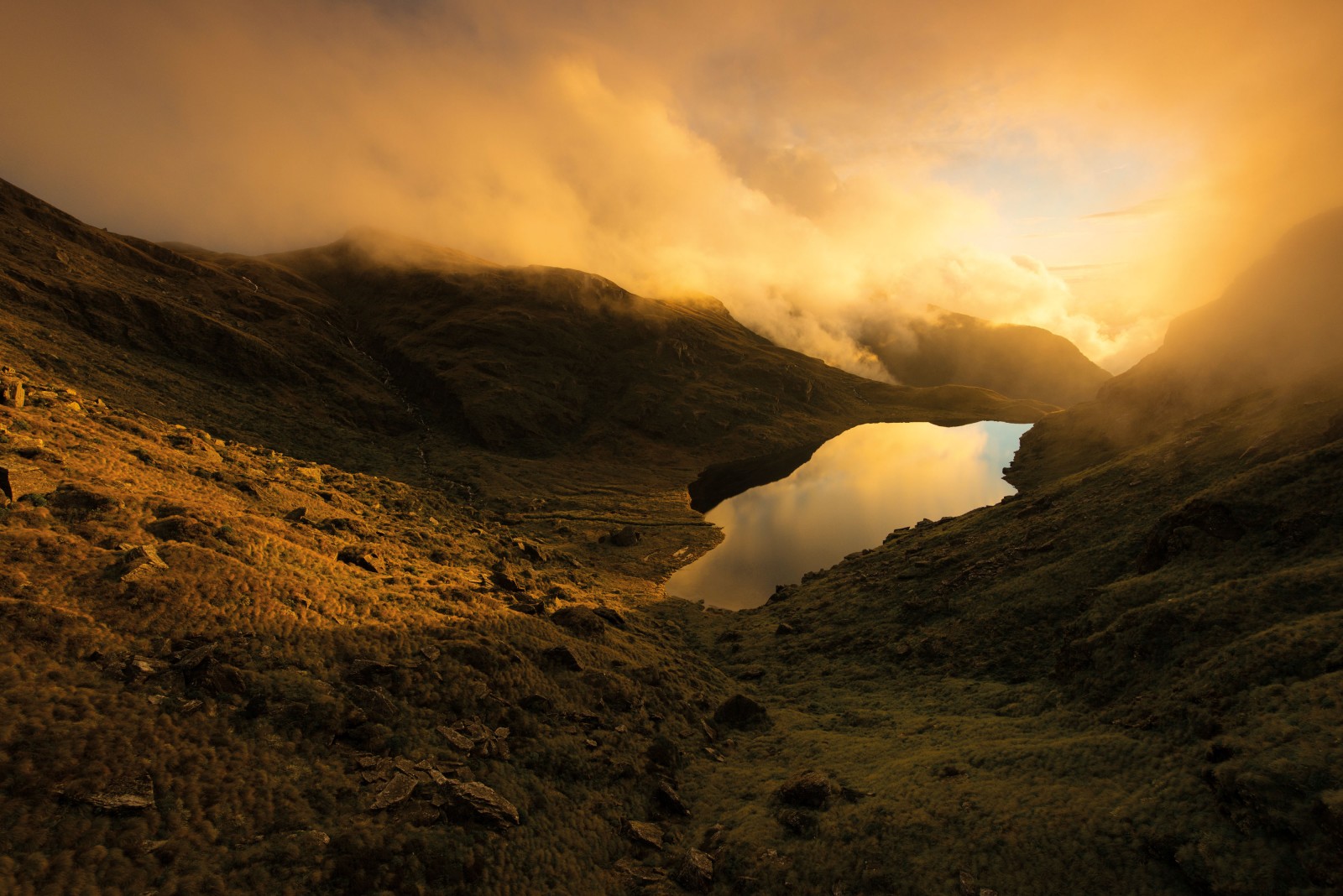 Ubiquitous West Coast cloud parts to illuminate Minim Mere—shaped like a musical note on a topographical map—high on the Haast Range. The mere (a shallow, flooded area of glacial till) is drained by Tuning Fork Creek and flows on down to the Arawhata River.